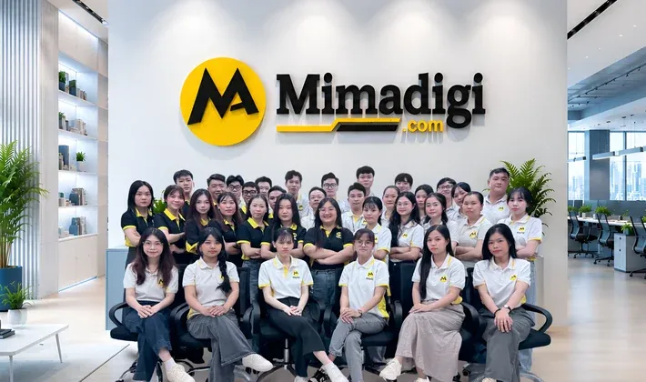 Nhân sự MIMA ngồi thành nhiều hàng trước bảng hiệu MIMA trong văn phòng